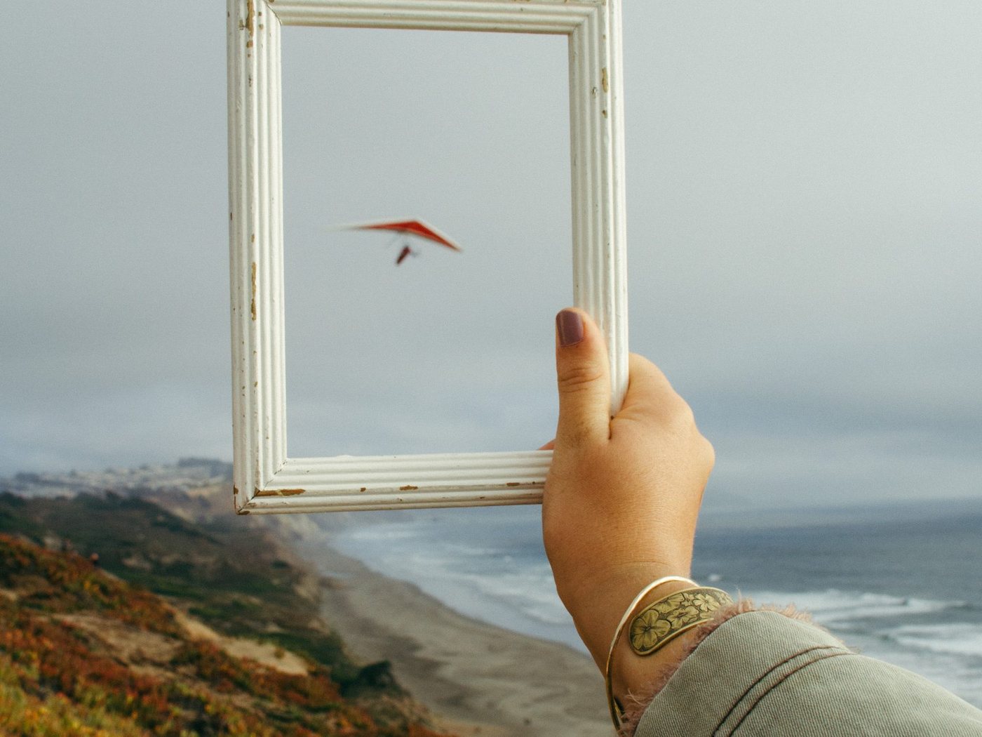 A hand holding an empty picture frame up against a coastal landscape